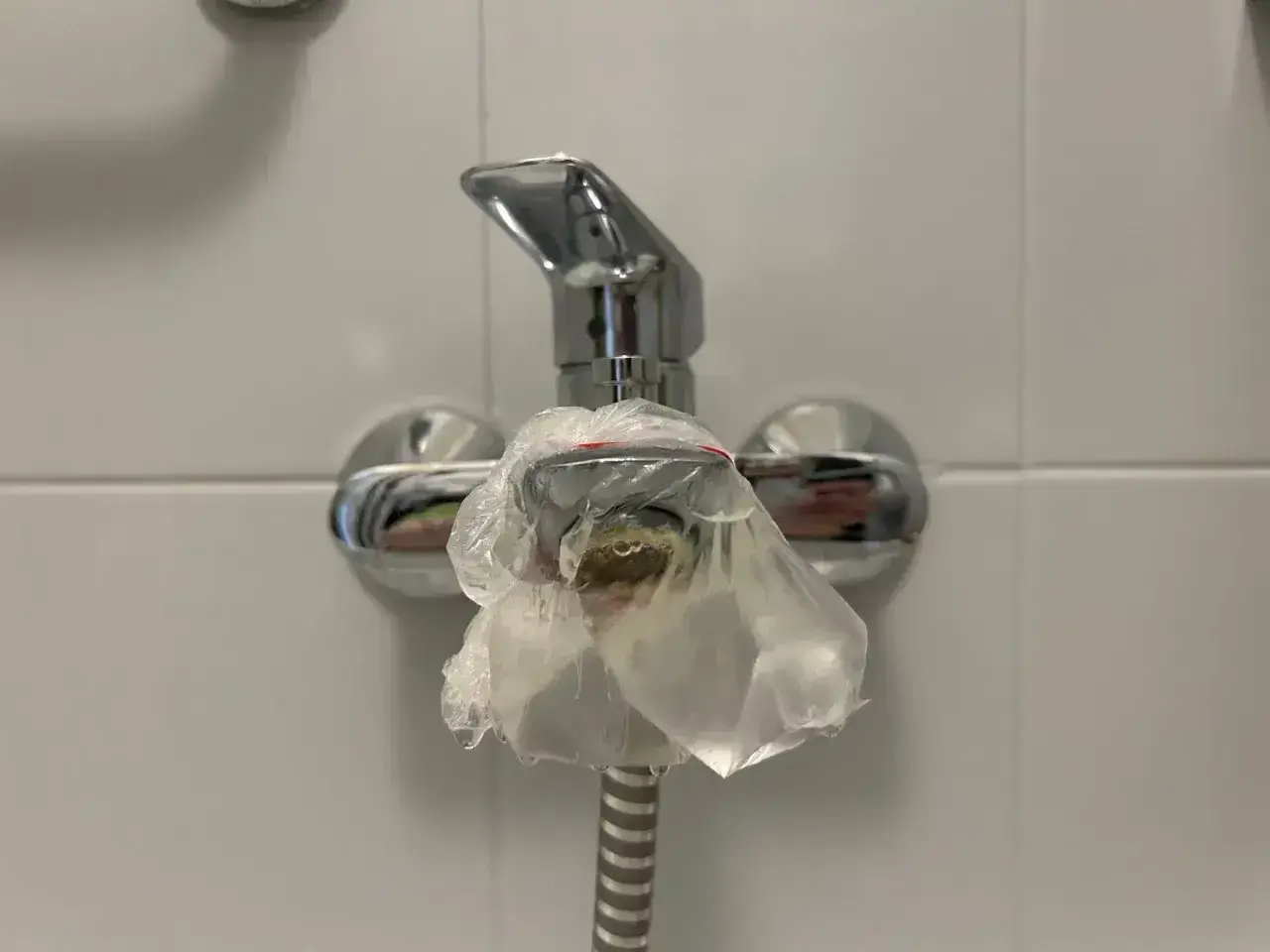 Kran prysznicowy owinięty folią, bo w bloku brak ciepłej wody. Krople zimnej wody spływają po opakowaniu.