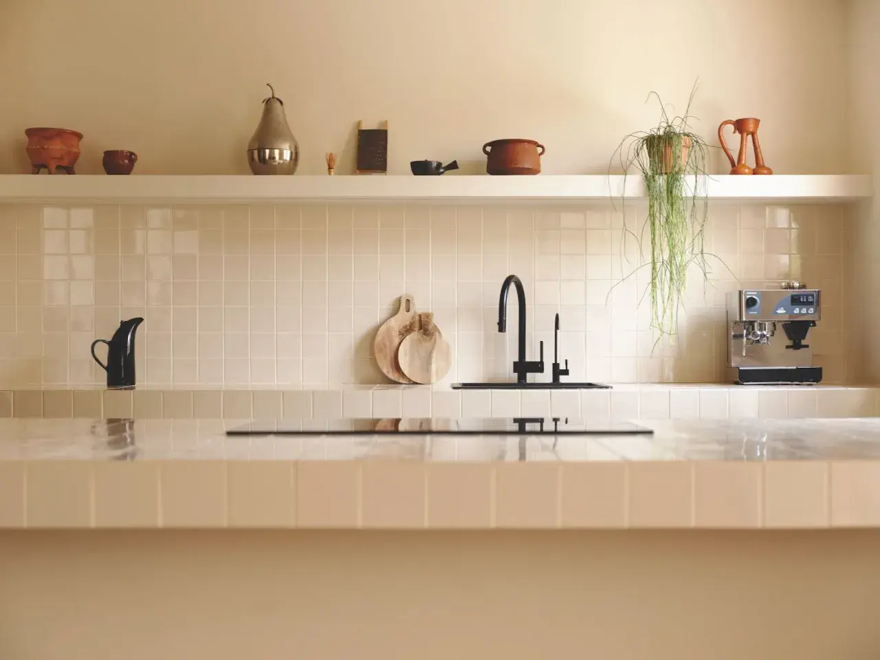 Encantadora cocina con azulejos claros, grifo negro y cafetera. Las últimas tendencias en azulejos para cocinas se reflejan en este diseño minimalista y funcional.