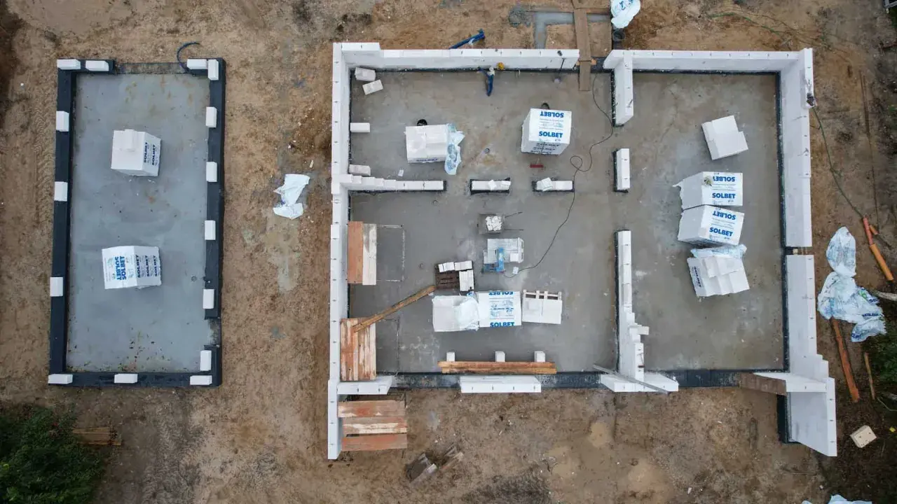 Budowa domu z bloczków betonowych. Materiały budowlane leżą na płycie fundamentowej, czekając na montaż ścian, by zapewnić niski współczynnik przenikania ciepła.
