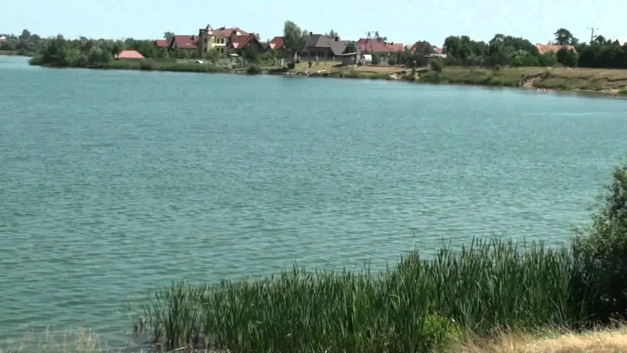 Spalona jezioro z domkami na brzegu. Woda jest turkusowa, a na pierwszym planie rośnie trzcina.