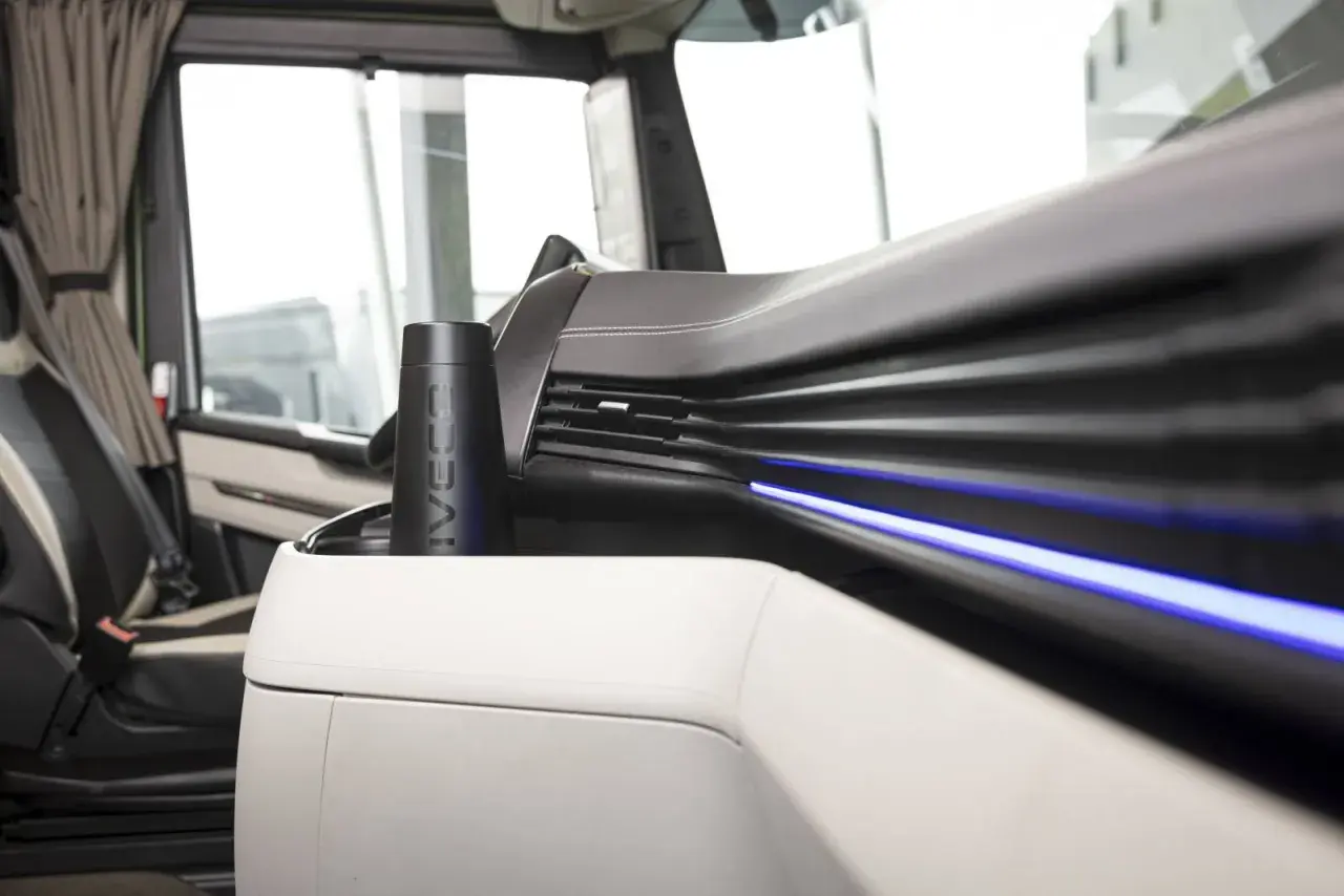 Un porte-gobelet noir avec le logo IVECO, un des indispensables du routier, est placé sur la console centrale d'un camion.