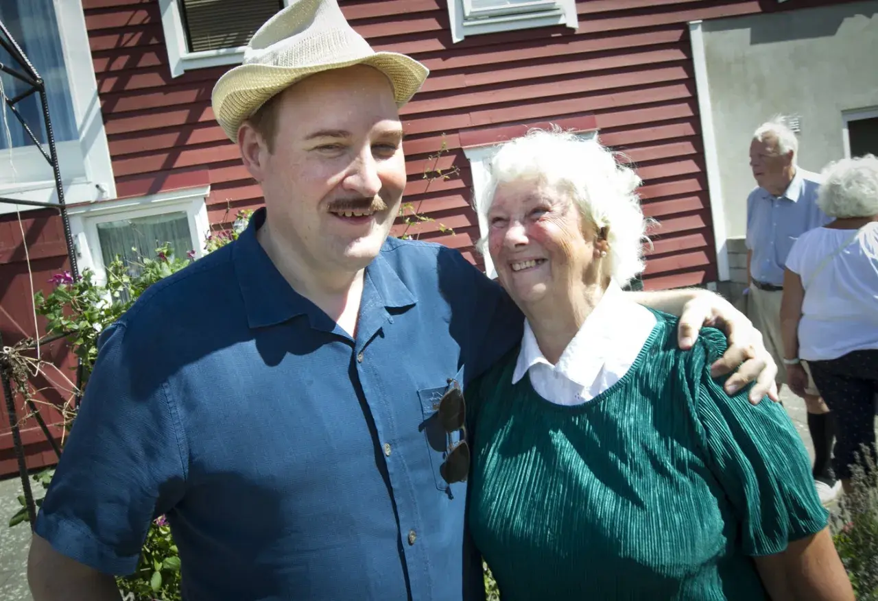 Sigge Dorsin ler mot kameran med en äldre kvinna. De står framför ett rött hus.