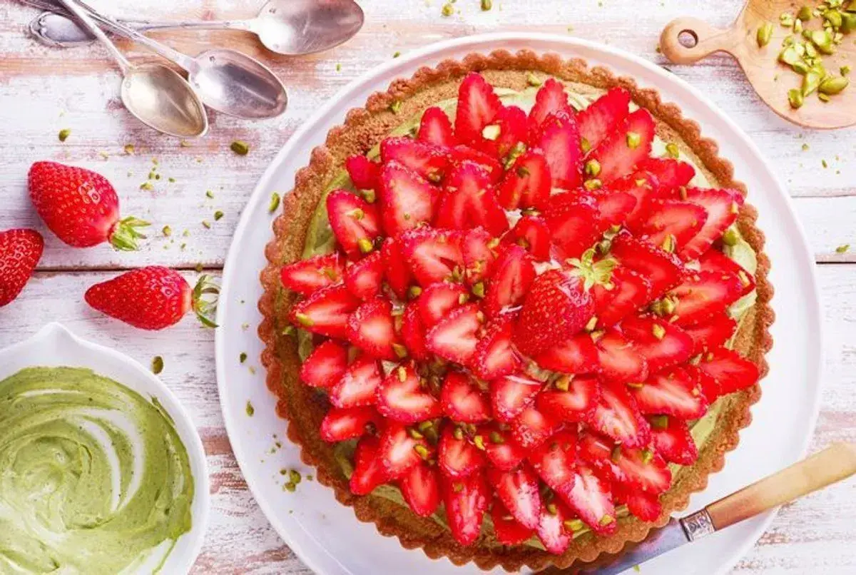 Tarte aux fraises sur pâte brisée, garnie d'une crème verte et de pistaches concassées. Un délice fruité et croquant.