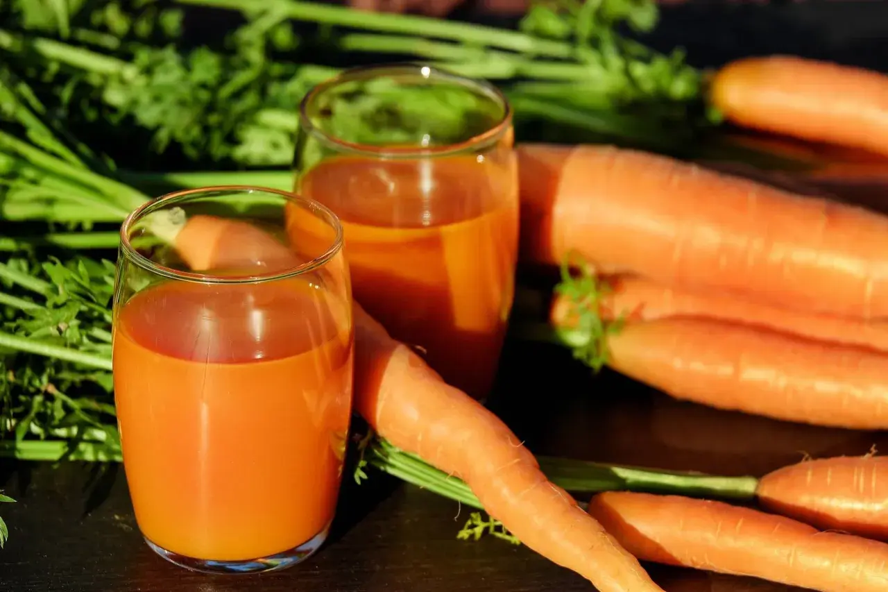 Frischer Karottensaft in Gläsern, umgeben von ganzen Karotten. Ein tolles Beispiel für vitamin a welche lebensmittel.