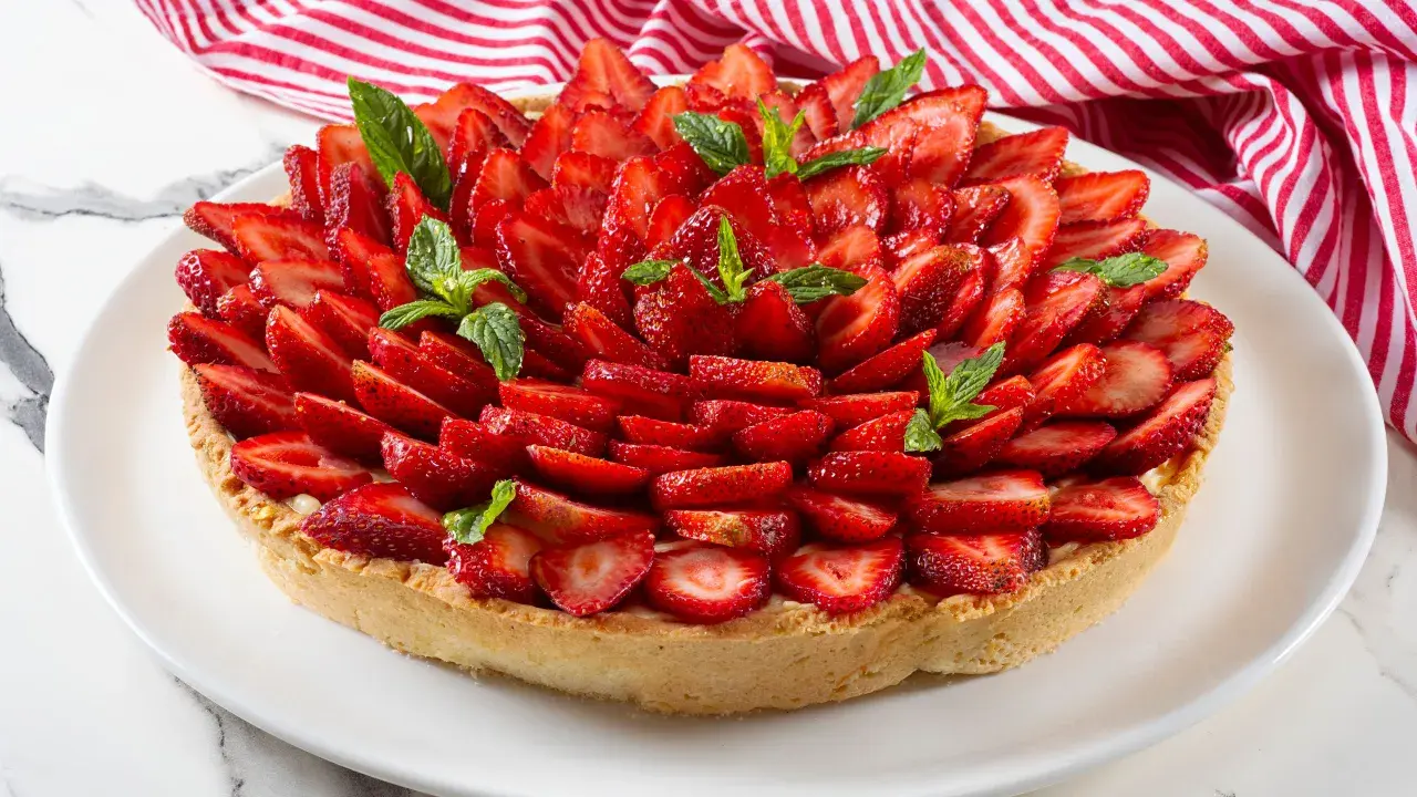 Deliziosa crostata alla crema, ricoperta da fragole fresche affettate e guarnita con foglie di menta.