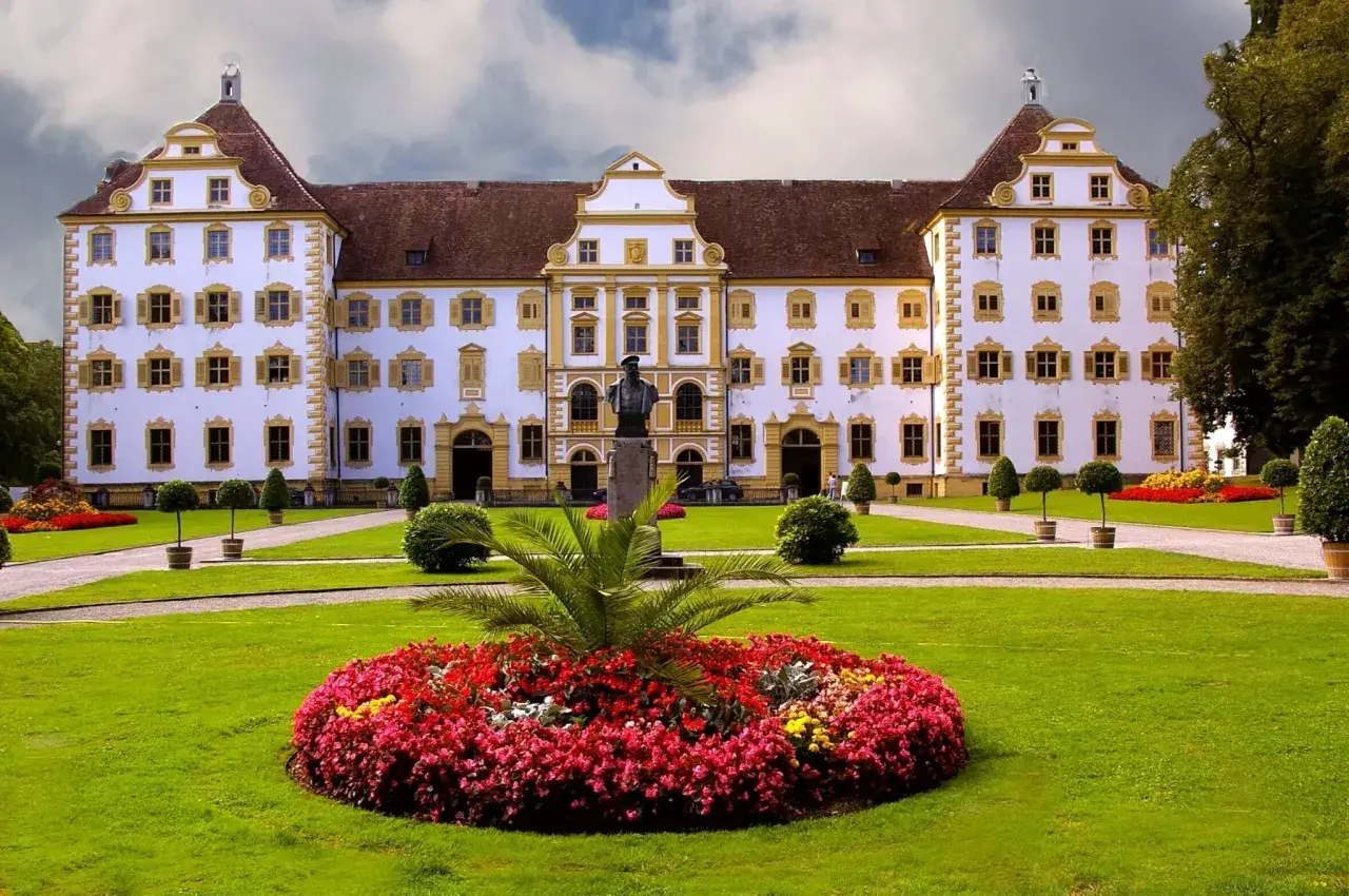 Prachtvolles Schloss Salem mit symmetrischer Fassade, gelben Akzenten und einem gepflegten Garten voller Blumen und Bäume.