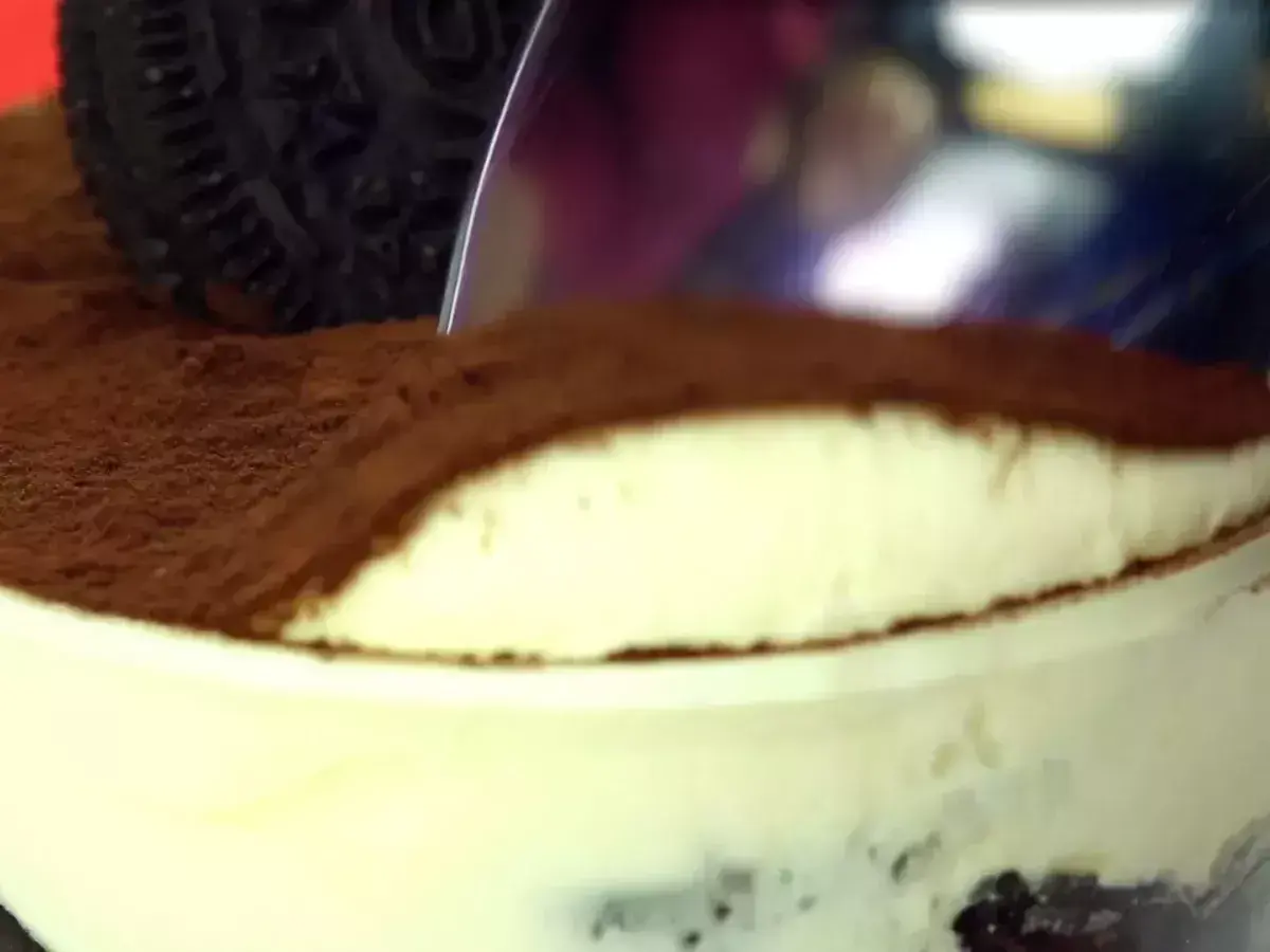 Une cuillère plonge dans un délicieux tiramisu Oreo, saupoudré de cacao. Un dessert gourmand à savourer !