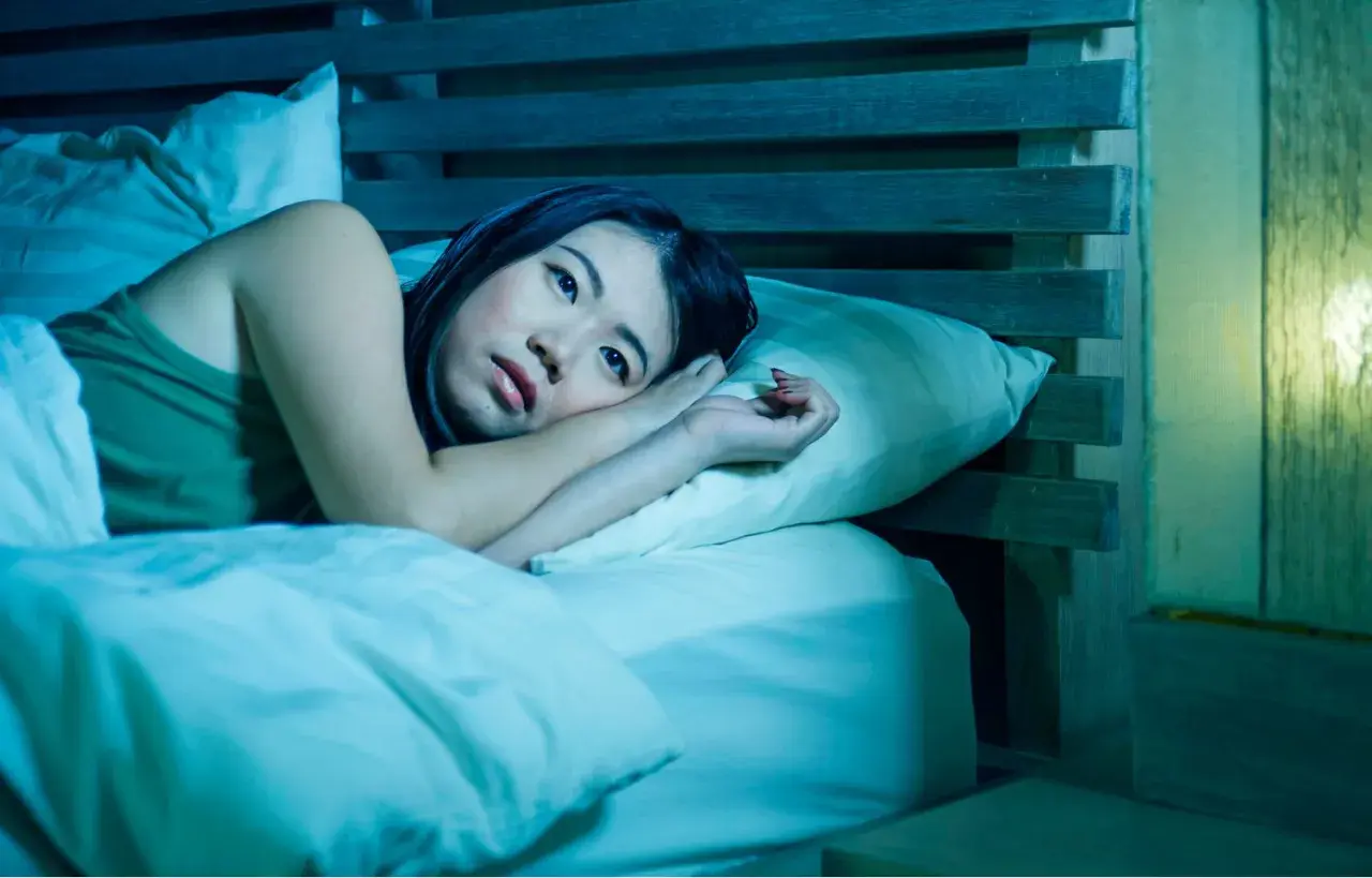 A woman lies awake in bed, her eyes wide open, a picture of paradoxical insomnia. The room is bathed in a cool, blue light, emphasizing her distress.