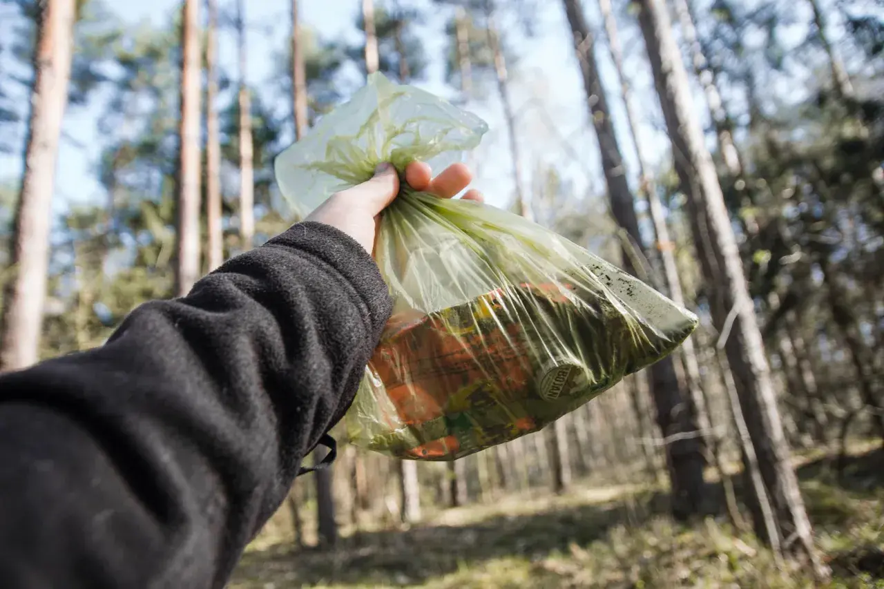 Ręka trzyma worek ze śmieciami w lesie. Zasady "leave no trace" to dbanie o przyrodę.