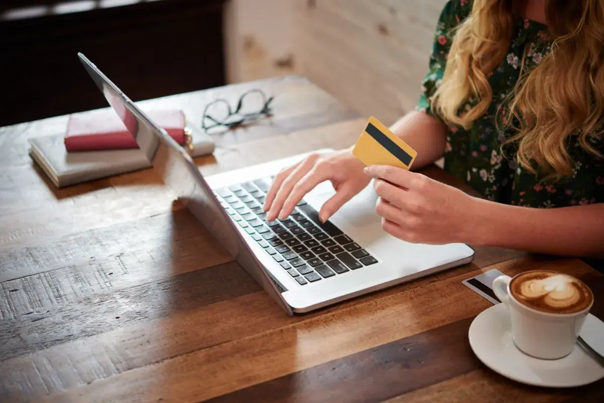 Kobieta z kartą płatniczą na laptopie, szukająca pożyczki dla każdego bez odmowy. Kawa obok.