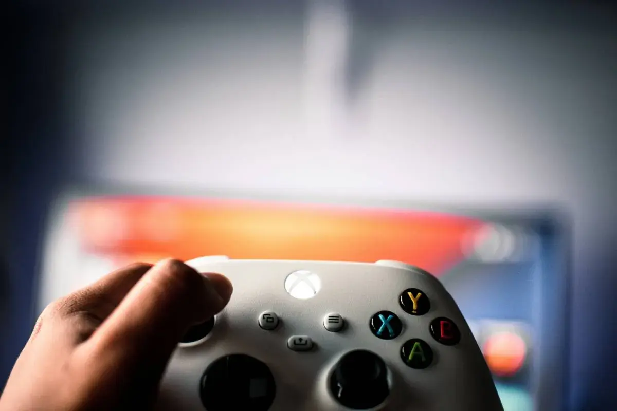 Dłoń trzyma biały kontroler Xbox, gotowa do gry. Wiedza to potęga, podobne gry wymagają strategii i refleksu.