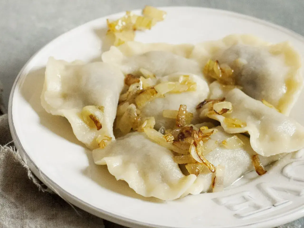 Pyszne pierogi z kapustą i skwarkami, ułożone na białym talerzu, kuszą swoim domowym wyglądem.