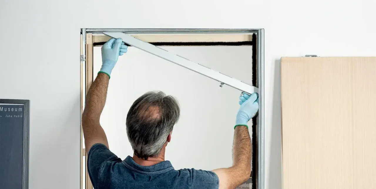 Installazione controtelaio porta scorrevole in cartongesso. L'operaio con guanti azzurri posiziona la guida superiore.
