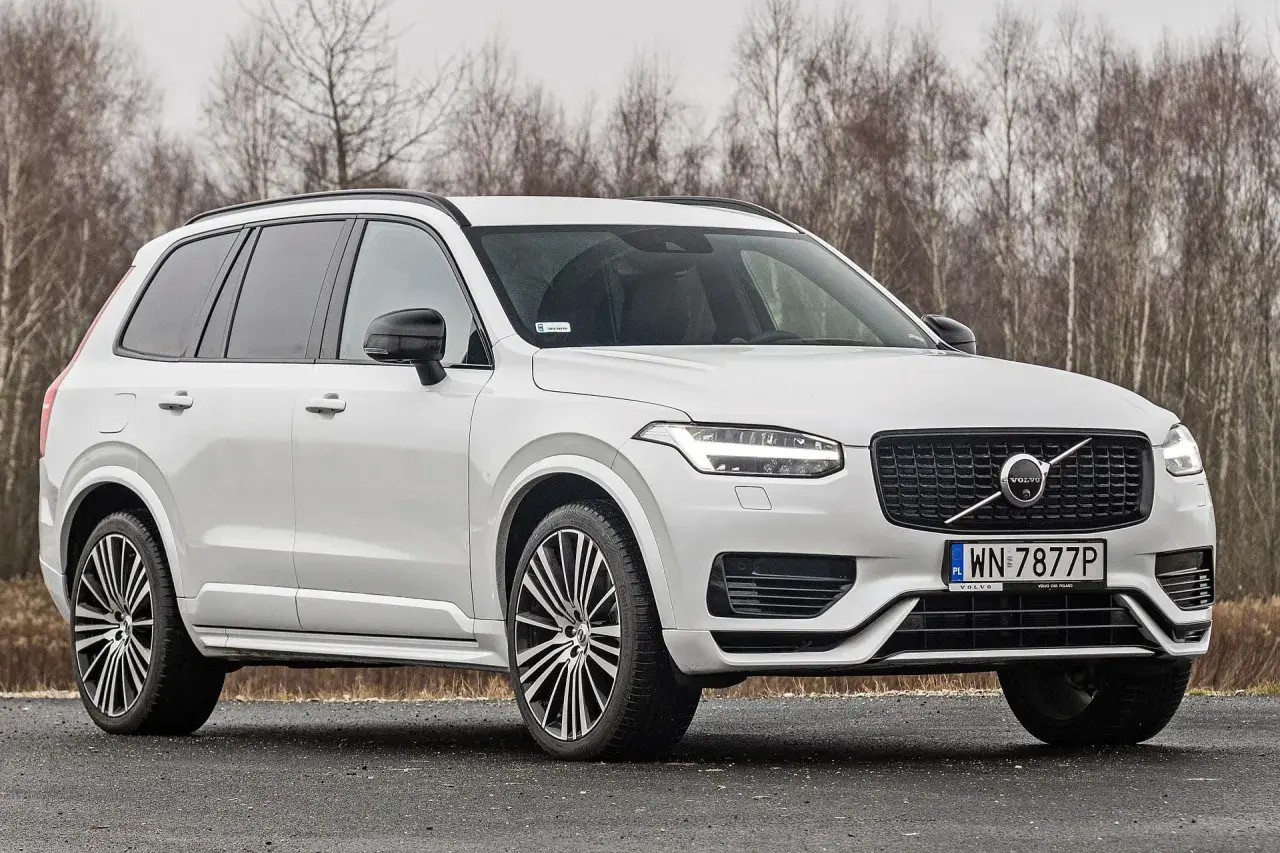 Białe Volvo XC90 T6 z czarnymi felgami stoi na drodze, za nim las.
