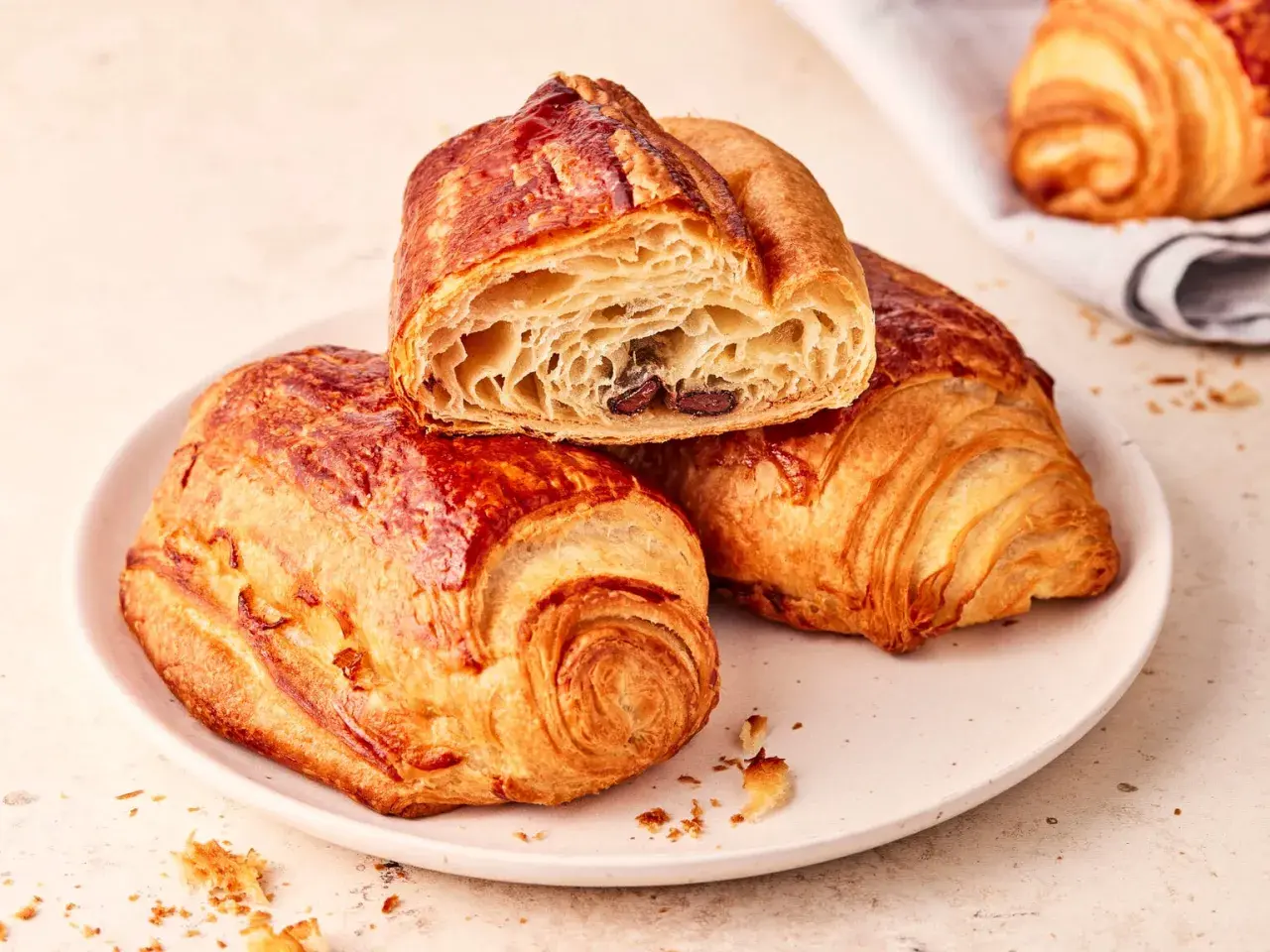 Zwei goldbraune, knusprige Pain au Chocolat auf einem Teller, eines davon angeschnitten, enthüllt die schokoladige Füllung.