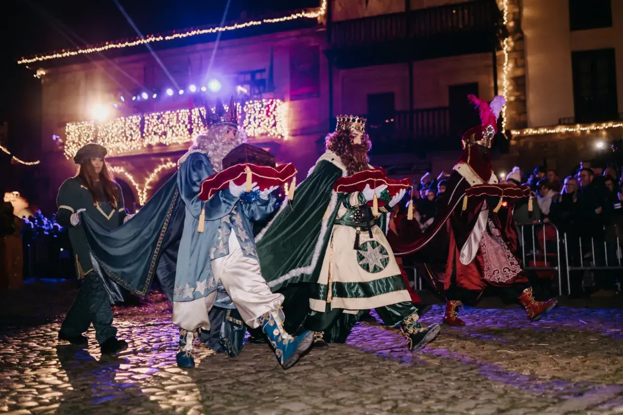 Los Reyes Magos desfilan en la cabalgata de Santillana del Mar, portando regalos bajo luces festivas.