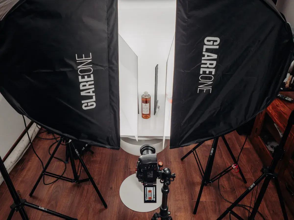 Profesjonalna fotografia produktowa jak zacząć? Zestaw oświetleniowy z dwiema lampami Glareone, aparatem i butelką w tle.