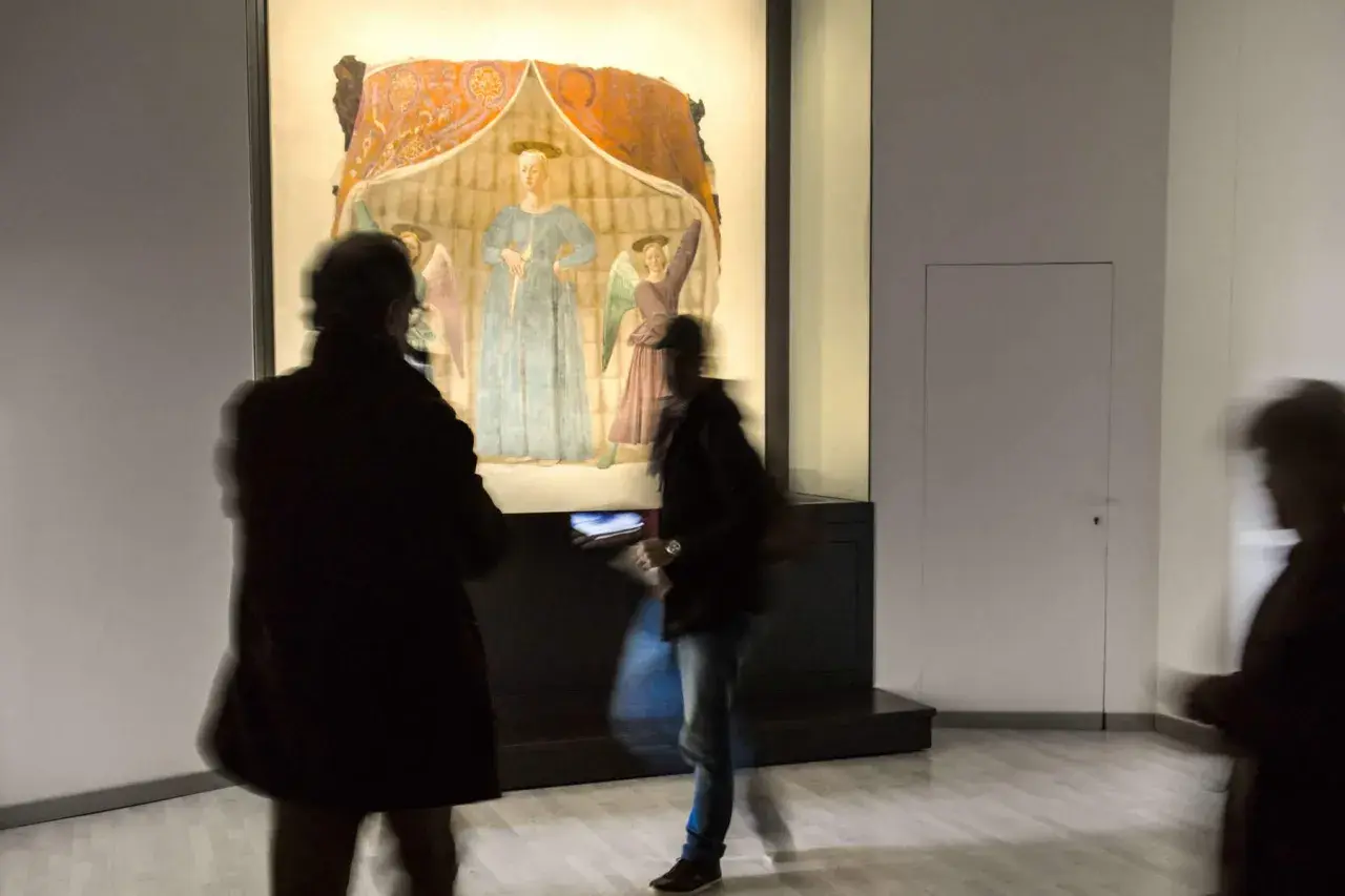 La Madonna del Parto di Piero della Francesca, con visitatori che la ammirano in un museo.