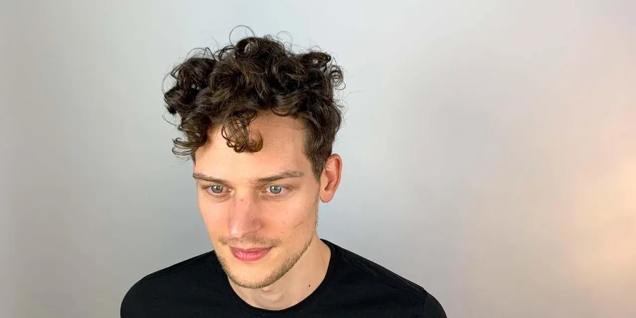 Junger Mann mit vollen, dunklen Locken. Ein Beispiel, wie bekommt man locken jungs für einen coolen Look.