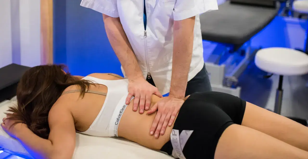 Un professionnel effectue un massage musculaire sportif sur le dos d'une femme allongée sur une table de massage.