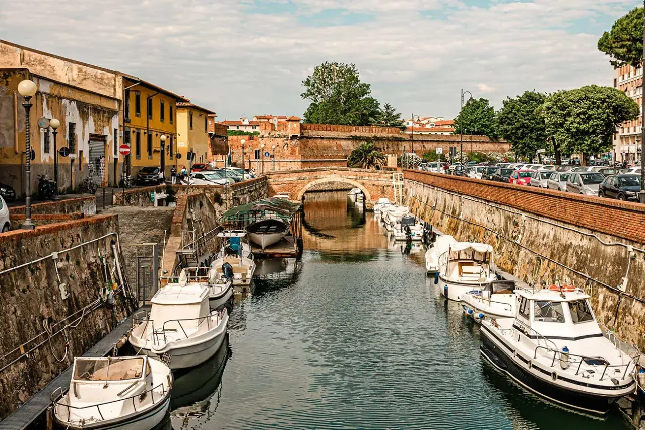 Boats docked along a canal in Livorno, Italy, with a brick bridge in the background.