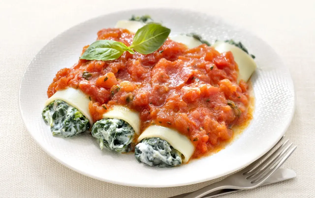 Cannelloni ricotta épinard généreusement nappés de sauce tomate, garni d'une feuille de basilic. Un plat savoureux et réconfortant.
