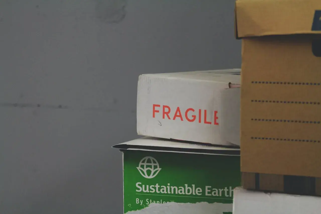 Paczka przyjęta w oddziale. Na białym kartonie napis "FRAGILE", pod nim zielony z napisem "Sustainable Earth". Obok brązowe pudło.
