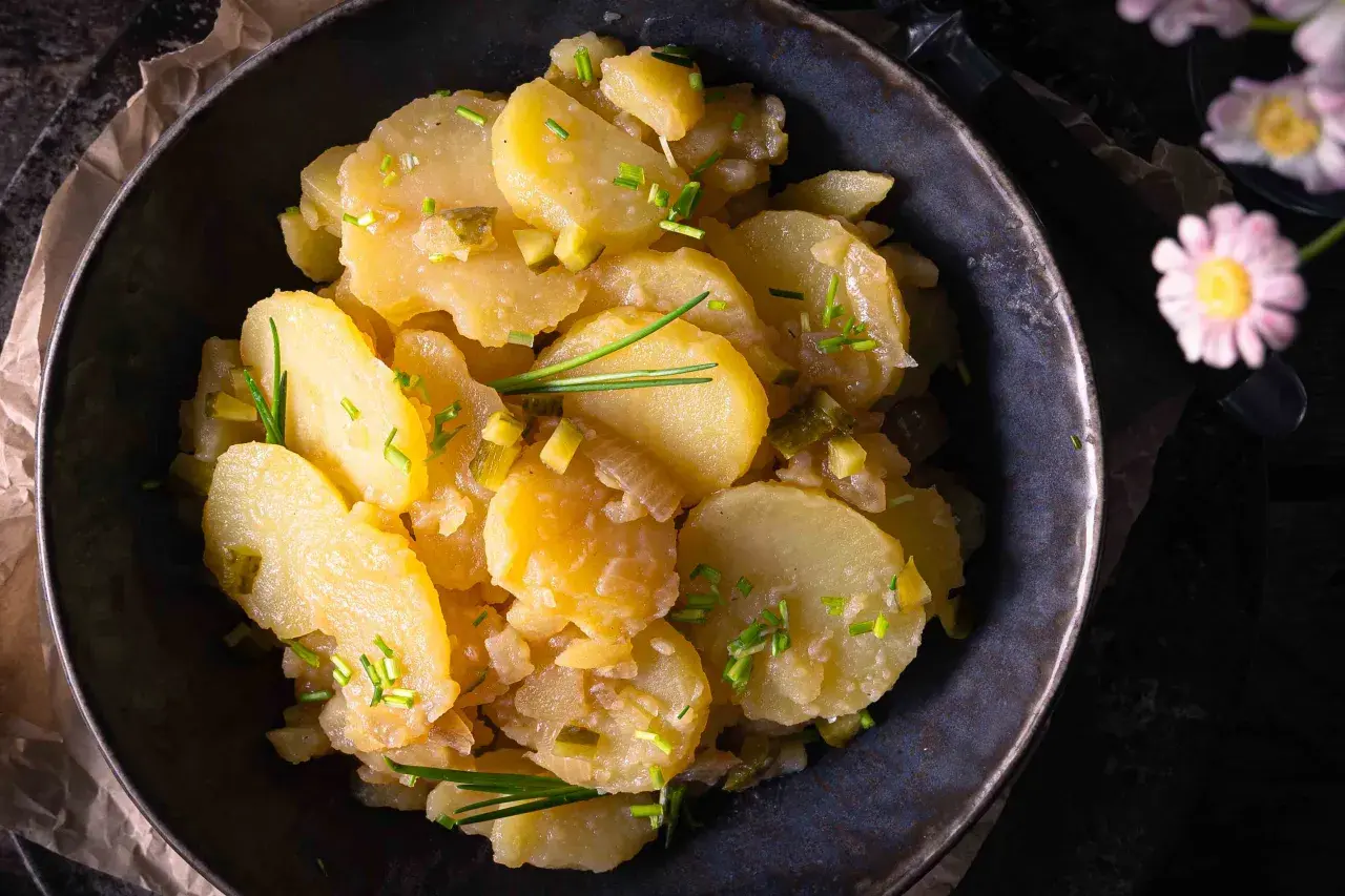 Schüssel mit Kartoffelsalat ohne Mayo, garniert mit Schnittlauch und Gurkenstückchen.