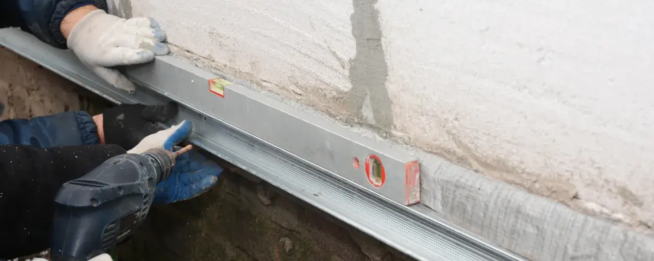 Handwerker montieren mit Wasserwaage und Bohrmaschine eine Horizontalsperre aus Blech an einer Wand.