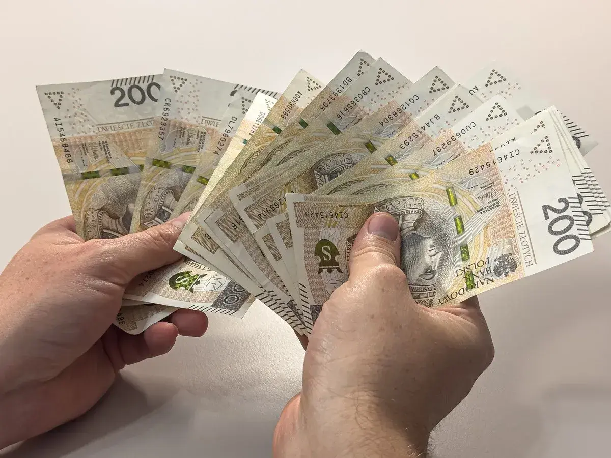 Dwie ręce trzymają wachlarz banknotów po 200 złotych. Czy to duł, czy dół, ważne, że pieniądze są!