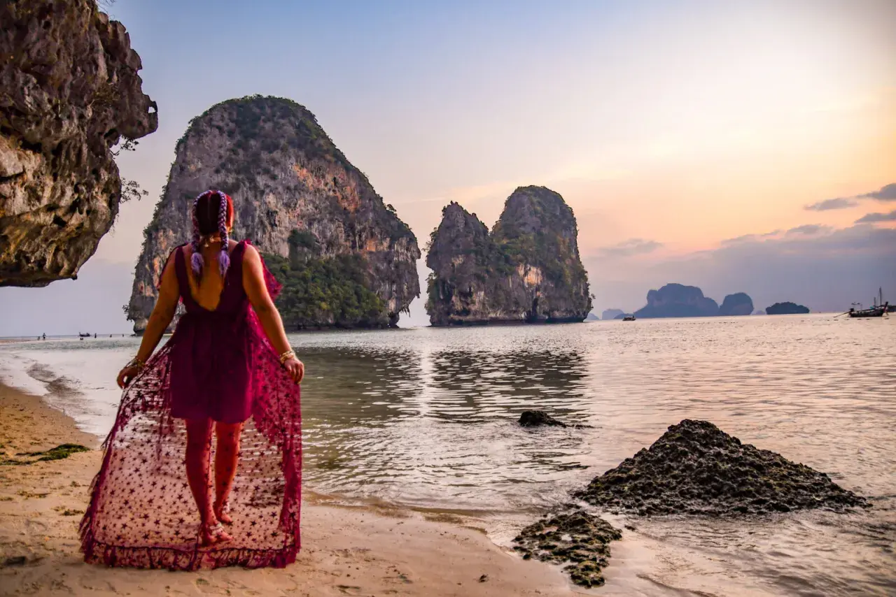 Kobieta w zwiewnej sukience spaceruje po plaży Ao Nang, podziwiając skaliste wysepki o zachodzie słońca.