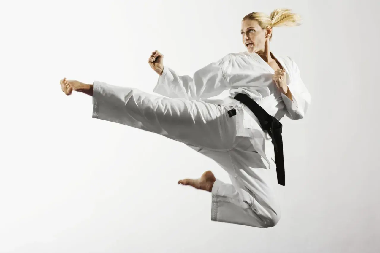 Kobieta w białym karate gi wykonuje wysokie kopnięcie w powietrzu.