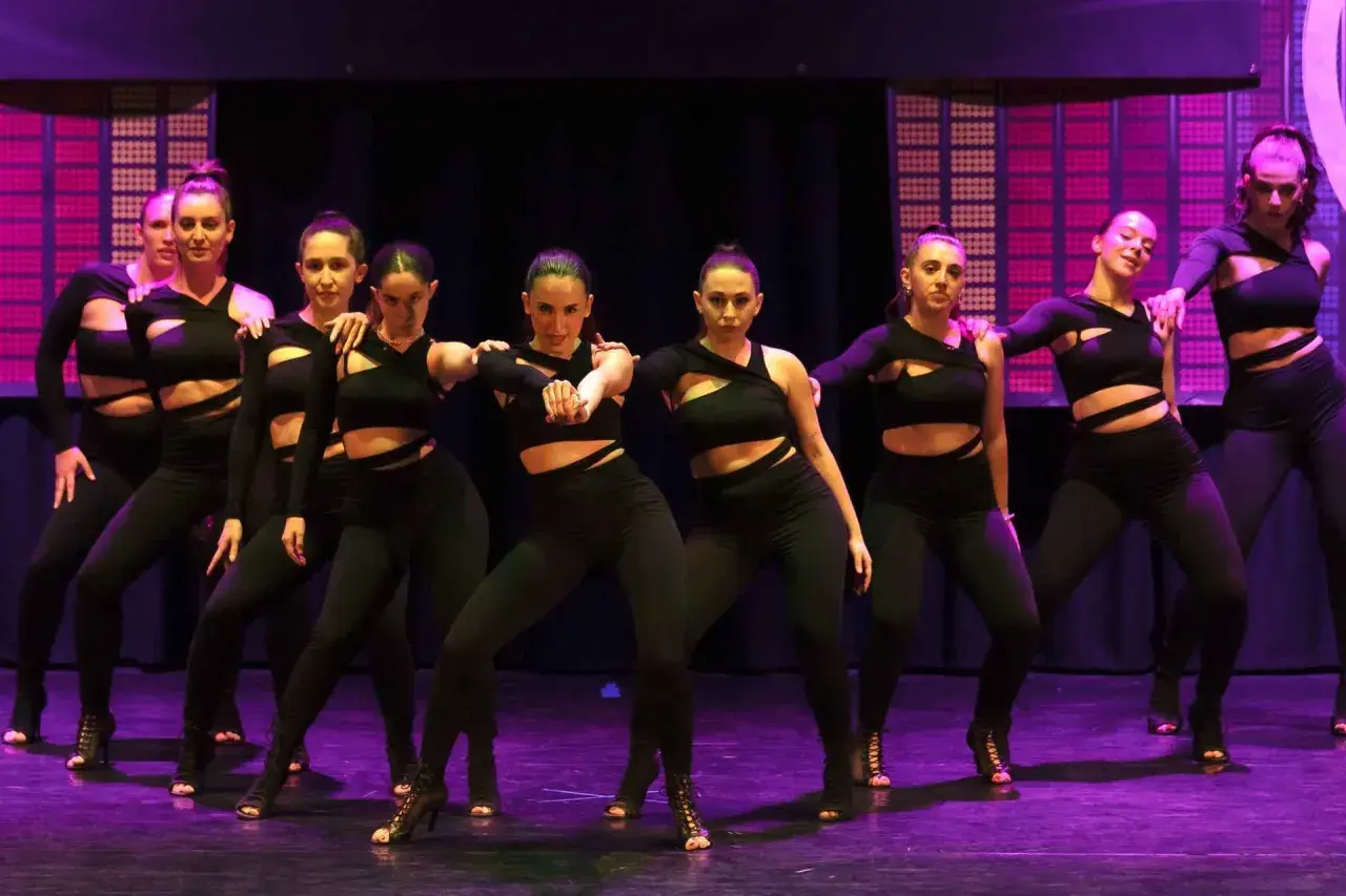 Un gruppo di ballerine in abiti neri si esibisce su un palco illuminato, creando un'atmosfera da dance hall.