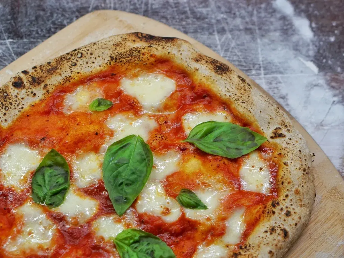 Une Margherita parfaite, symbole de la recette pizza italienne traditionnelle. Sauce tomate, mozzarella fondante et basilic frais sur une pâte dorée.