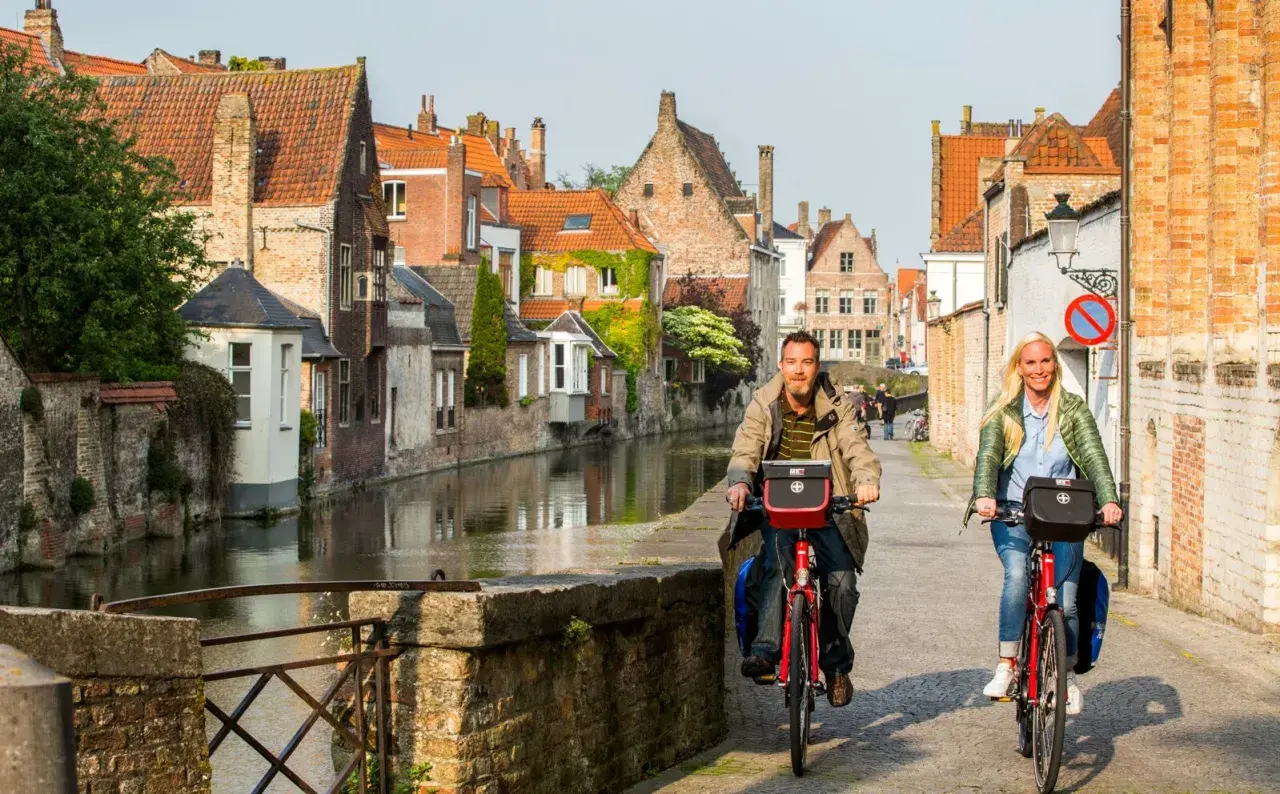 Couple enjoying a Bruges bike tour along a canal, with historic buildings lining the waterway.