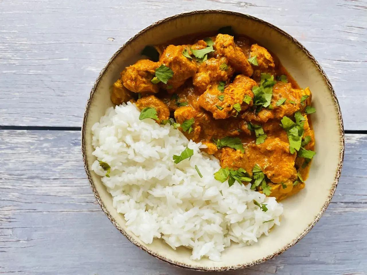 Aksamitny kurczak tikka masala w kremowym sosie, podany z puszystym ryżem i posypany świeżą kolendrą.