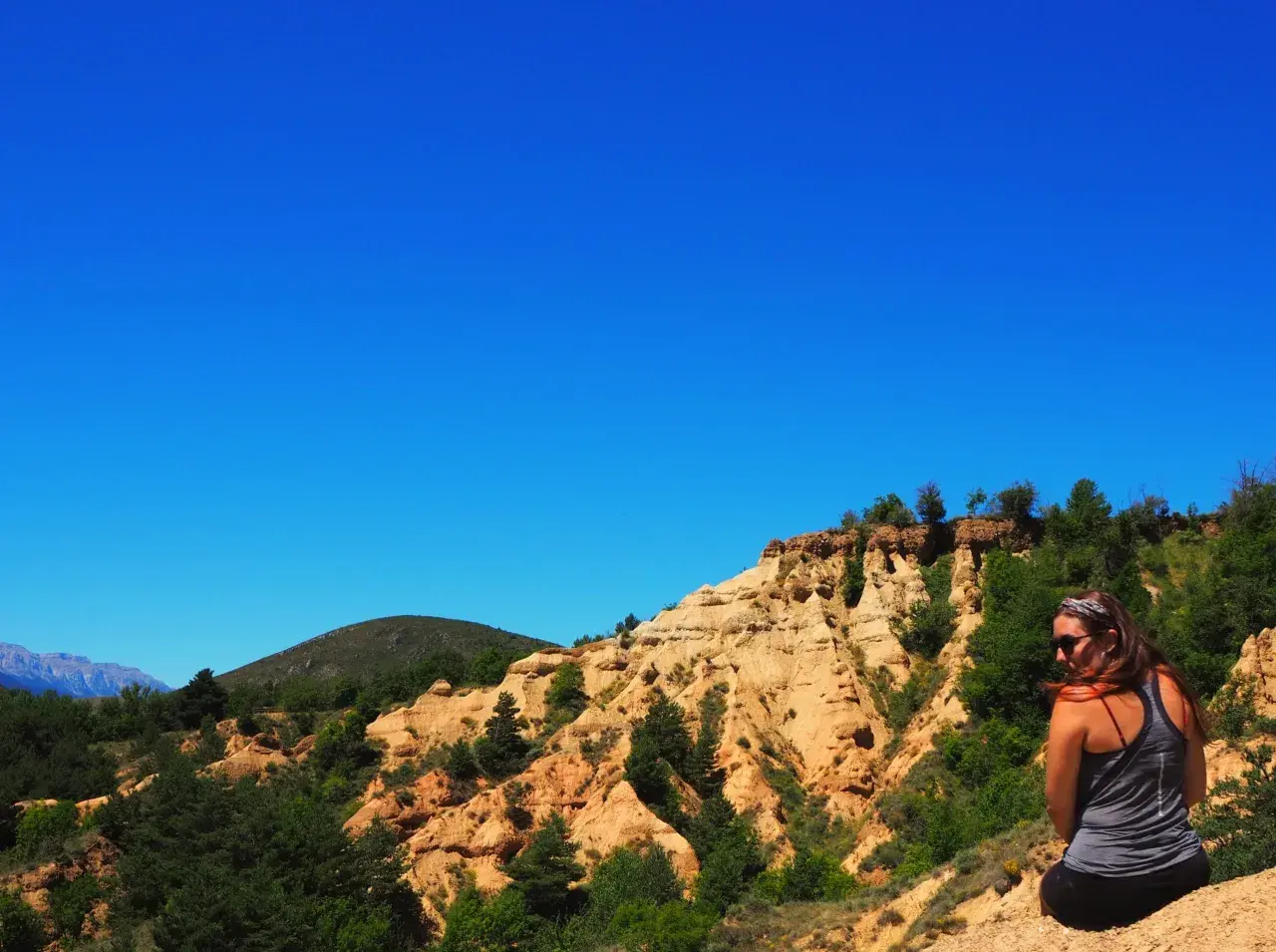 Una mujer contempla el paisaje de la Cerdanya, con sus formaciones rocosas ocres y vegetación verde bajo un cielo azul intenso.