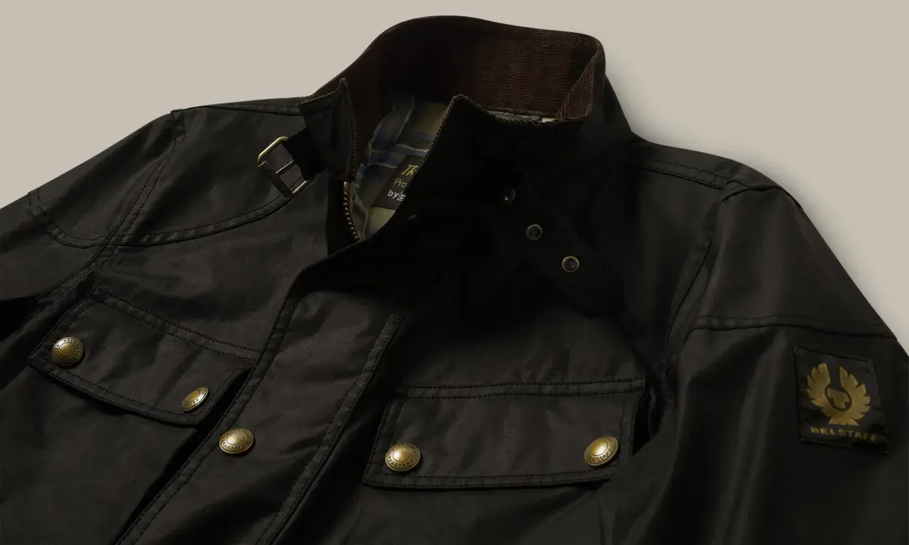 Chaqueta Belstaff negra, lista para limpiar en casa. Detalles de bolsillos, cremallera y logo dorado.