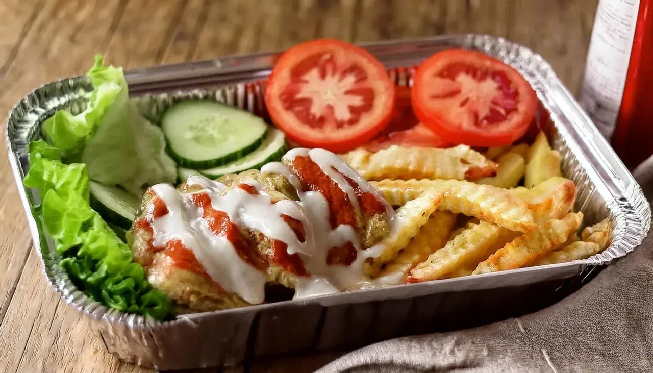 Pyszny kapsalon przepis z frytkami, mięsem, sałatą, pomidorem i ogórkiem, polany sosem.