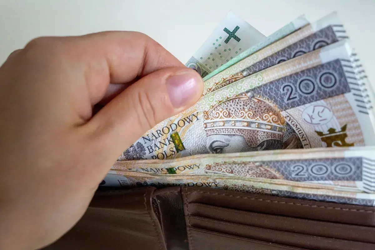 Dłoń wkłada polskie banknoty 200 zł do portfela. Zastanawiasz się, ile wynosi składka zdrowotna?