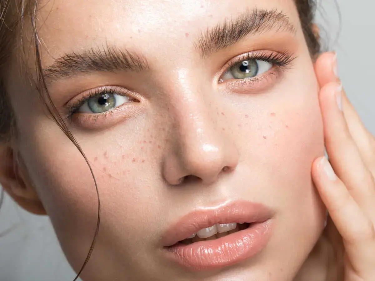 Un visage de femme aux yeux verts et aux taches de rousseur. La poudre libre matifie et fixe le maquillage pour un teint parfait.