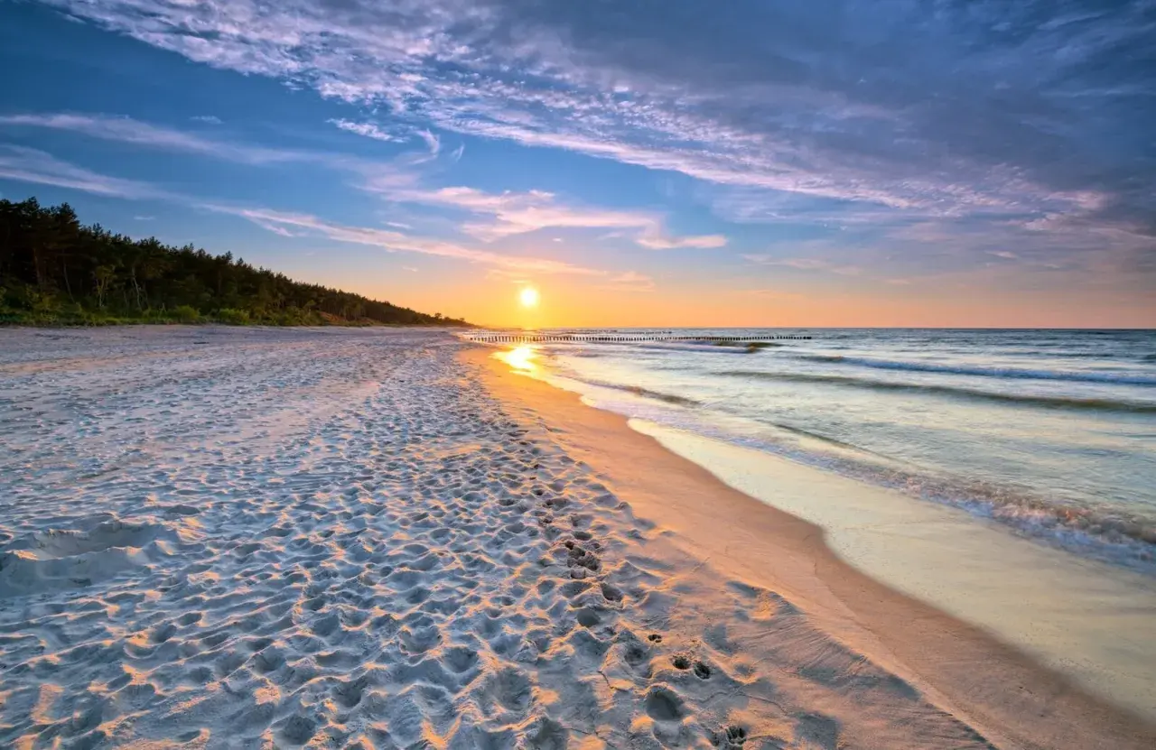 Zachód słońca nad morzem, piaszczysta plaża z śladami stóp, las w tle. Idealne, fajne miejsce nad morzem dla dwojga na romantyczny spacer.