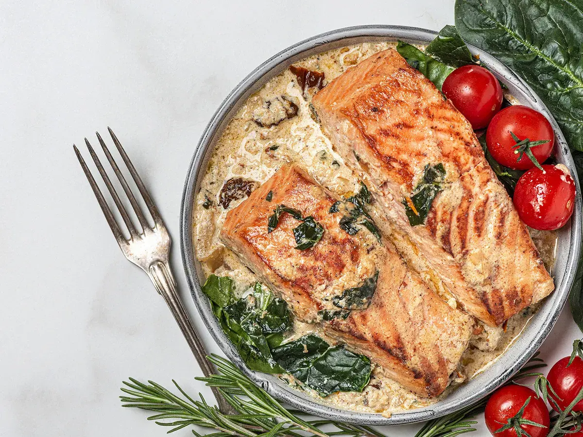 Deux pavés de saumon grillé dans une sauce crémeuse aux épinards, accompagnés de tomates cerises. Une recette saumon parfaite pour un dîner savoureux.