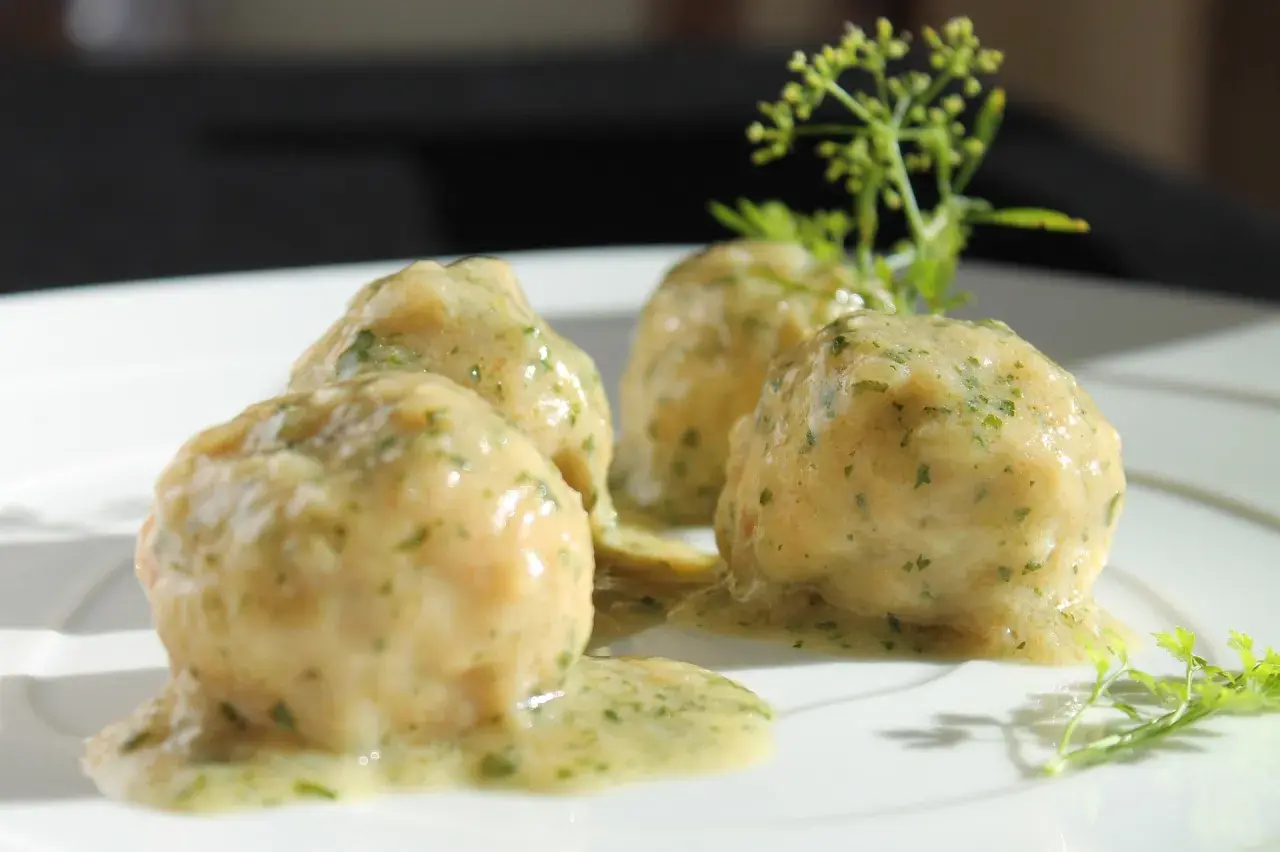 Quattro polpette in umido, ricoperte da una salsa cremosa alle erbe, servite su un piatto bianco con guarnizione di prezzemolo.