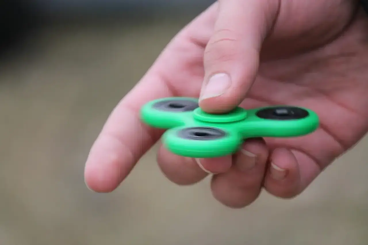 Groene fidget spinner in hand, een hulpmiddel voor concentratie bij hoog functionerend autisme.