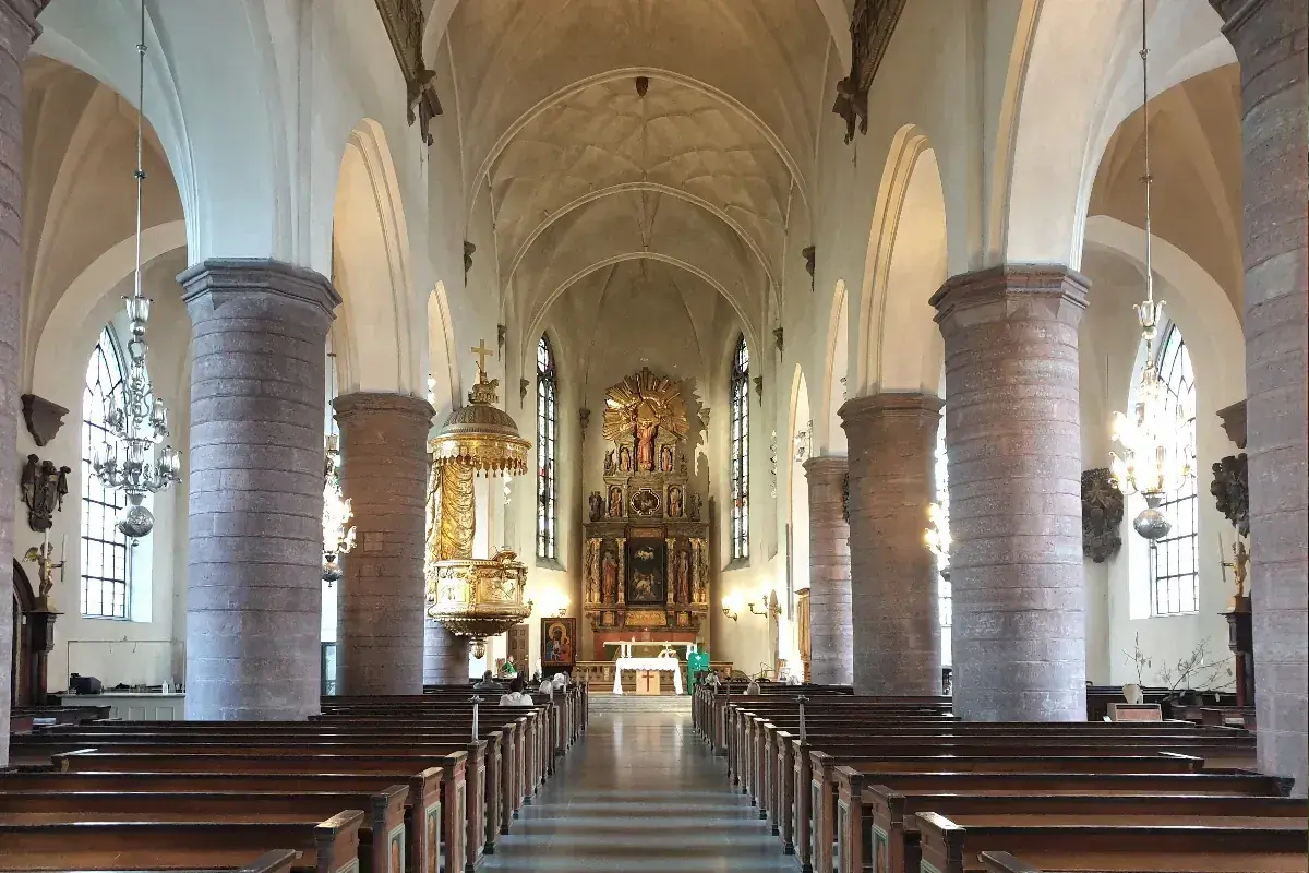 Interiör av St Jacobs kyrka med bänkar, pelare och altare.