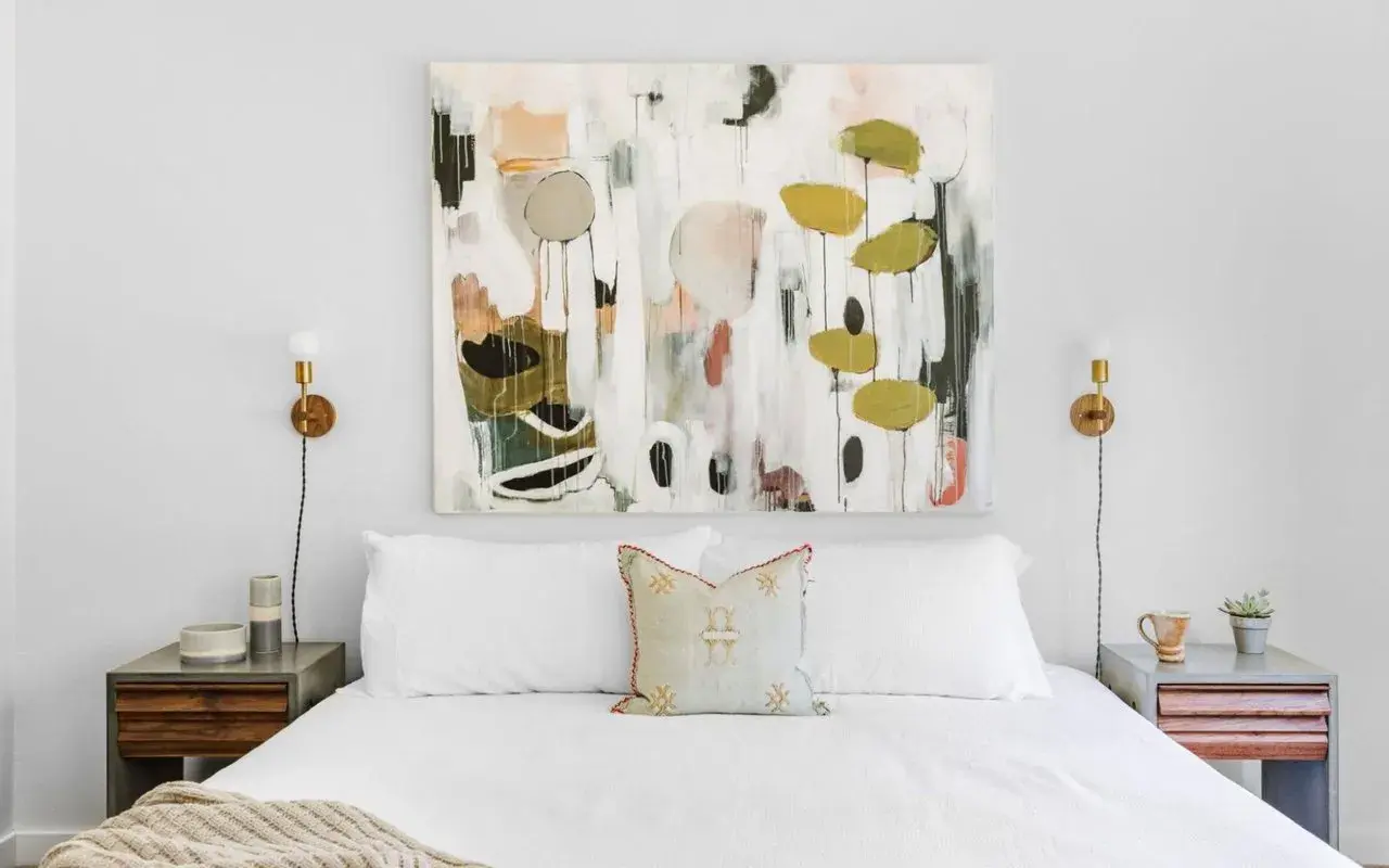 Staging a master bedroom with a large abstract painting above a white bed, flanked by modern nightstands and sconces.