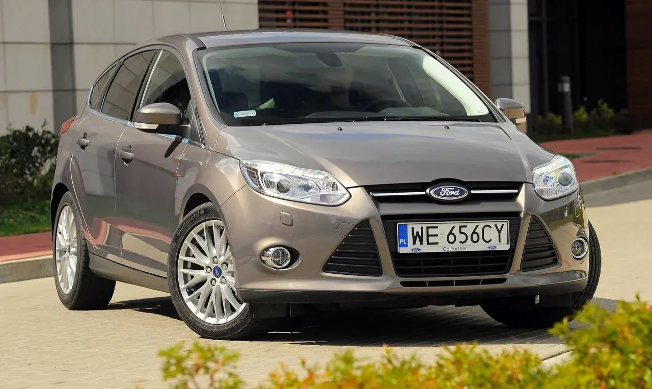 Brązowy Ford Focus 2014, zaparkowany przed nowoczesnym budynkiem, gotowy do podróży.