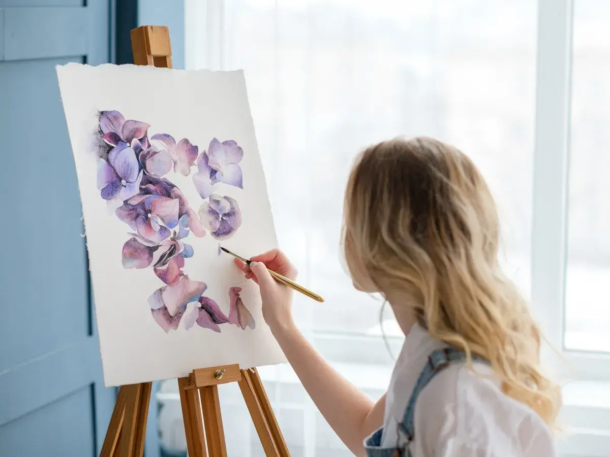 Kobieta maluje akwarelami fioletowe kwiaty. To inspiracja, jak być kreatywnym, tworząc piękno.