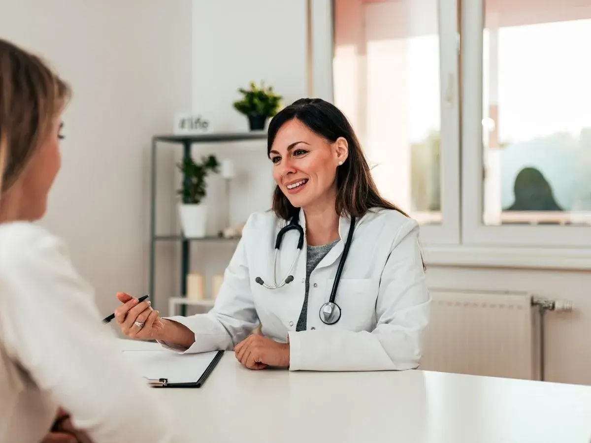 Medico sorridente parla con paziente, illustrando un punto con la penna. La scena evidenzia una buona comunicazione medico-paziente.